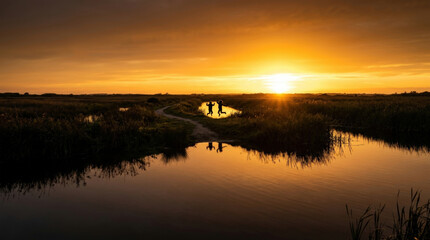 Fototapeta premium Pair of silhouetted explorers leap over marshy wetlands reflecting golden sun rays on calm water surface for conservation storytelling.