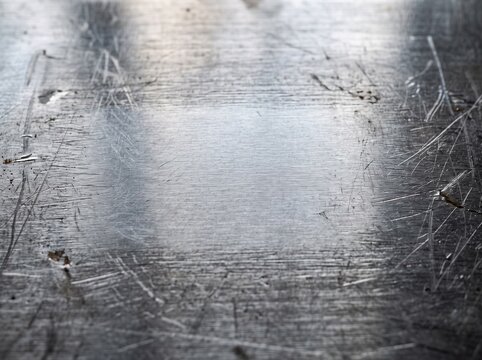 Close-up shot of a dark metallic surface with numerous scratches and a brighter worn area