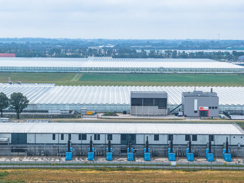 Aerial view of the Agriport A7 data center campus with industrial buildings, blue cooling units, and expansive glass greenhouses in the background in Middenmeer, Noord-Holland, Netherlands.