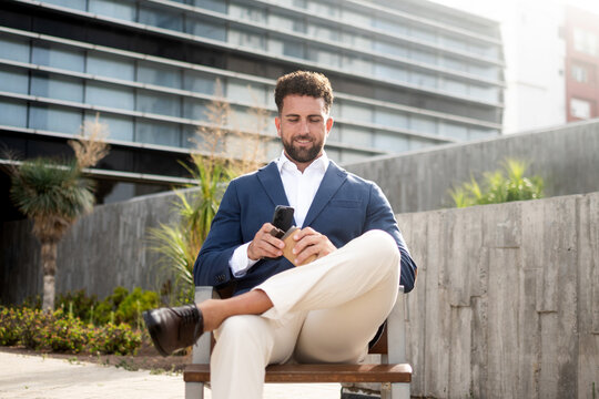 Businessman checking smartphone during coffee break outside office