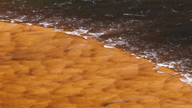 Rust-colored sediment plume curves into darker offshore sea as small waves break along the sharp boundary line.