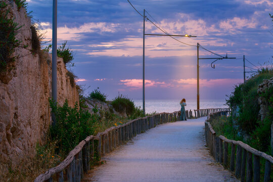 Woman in elegant dress on coastal path at sunset with dramatic sky romantic role play silhouette country side Wild West aesthetic under lantern lighting
