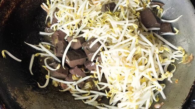 Dynamic close-up shot of a traditional Asian stir-fry process in a hot wok. Crisp, white bean sprouts are layered over savory cubes of congealed chicken blood tofu and garlic