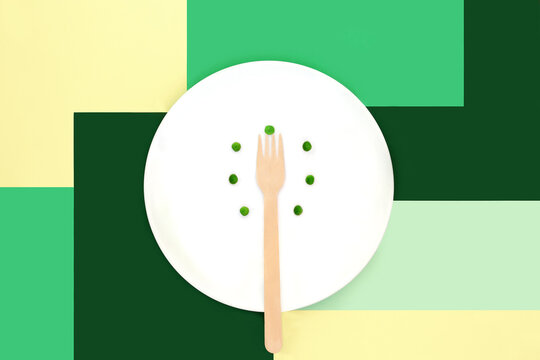 Extreme diet food culture concept, white plate, eco friendly wooden spoon, peas, surreal geometric design on green and cream.