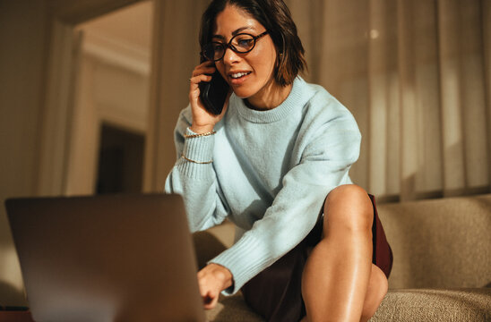 Woman talks on the phone while working on a laptop in her office