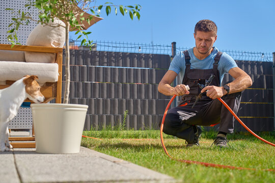 Man connecting garden hose to lawn sprinkler with dog nearby