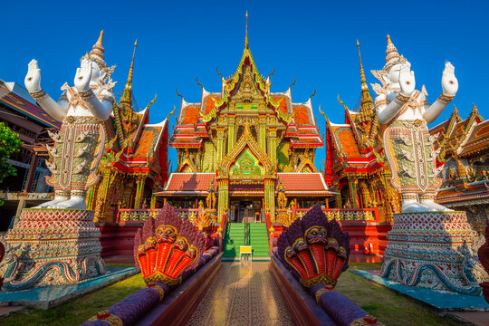 Stunning view of the golden main hall of Wat Si Uthumphon with giant white statues in Nakhon Sawan. The vibrant red and gold temple architecture is framed by multi-headed serpent sculptures.