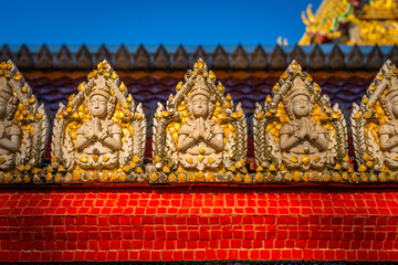 Fototapeta premium Close up of intricate celestial guardian relief sculptures along the red mosaic wall at Wat Sri Uthumphon in Mueang Nakhon Sawan District, Nakhon Sawan, Thailand, showcasing detailed Thai art.