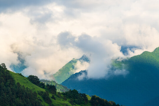 Clouds over the mountains and green hills at foggy sunset. Beautiful summer landscape.