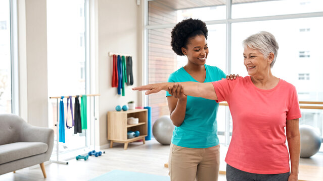 The healthcare professional is demonstrating and supporting a safe, simple mobility or stretching exercise while the senior woman follows the movement with a positive, confident smile.