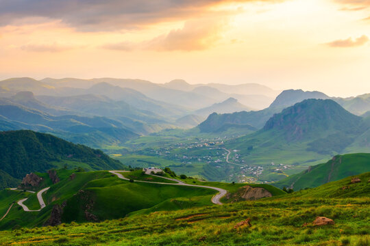 Gumbashi pass in North Caucasus, Russia. View of the green mountains and hills in the evening sunlight. Pink sky with clouds at sunset.