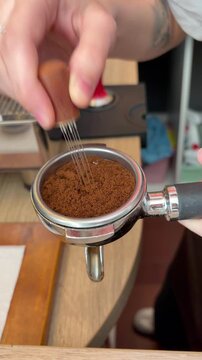 A barista uses a tool to distribute coffee grounds into a portafilter.