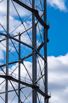 Steel lattice structure and industrial framework rising against bright blue sky and white clouds, emphasizing engineering detail and vertical geometry