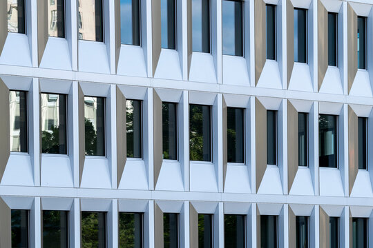 White modern building facade with deep vertical fins and dark window openings forming a precise geometric rhythm across contemporary architecture