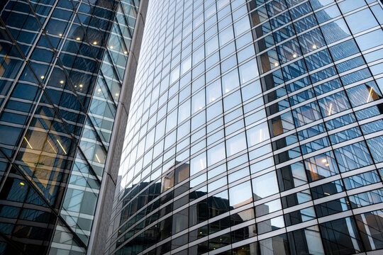 Upward view between modern glass towers with reflective facades, geometric window grids and converging lines in a dense urban architectural setting