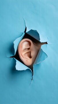 Human Ear Listening Carefully Through a Ripped Blue Paper Hole Discovering Secrets