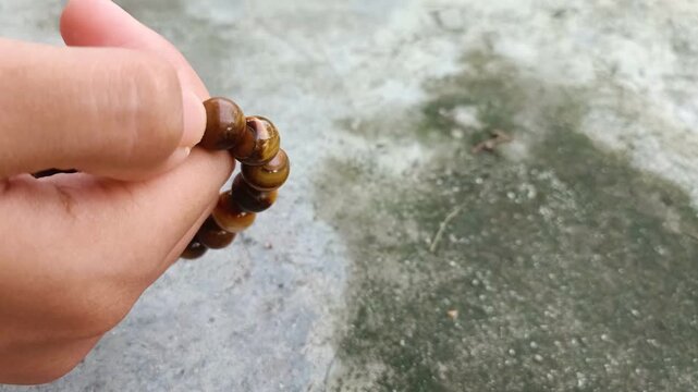 Close up of hand holding tiger eye stone bracelet on textured concrete background.
