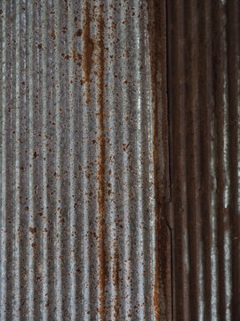 vertical composition focusing on the junction of corrugated iron sheets, featuring vertical rust streaks and weathered zinc finishes. The image presents visual elements of industrial architecture, rus