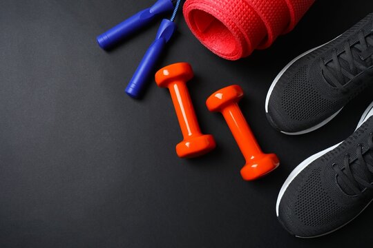 Flat lay of fitness equipment including sneakers, dumbbells, mat and jump rope on back background