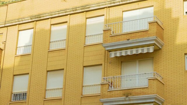 Urban housing in Spain with metal balcony railings and closed window shutters. Brick facade with physical security barriers. Home protection, vacant property security and squatter prevention