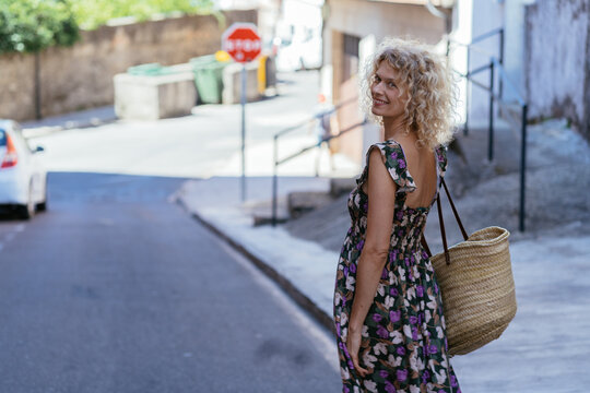 Smiling Blonde Woman Looking Back While Walking on Sunny Street During Summer Travel in Spain
