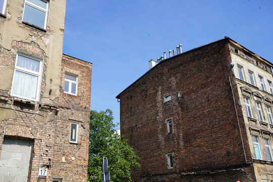 Wide street angle showing historic weathered brick tenement buildings and decaying facades in Gdansk, Poland, under a clear blue sky.