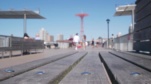 Coney Island beach, wooden pier promenade in Brooklyn, New York, United States. Boardwalk near retro luna park. Amusement park on ocean coast beach. People on waterfront summer holiday in NYC, USA.