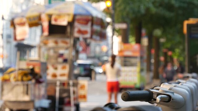 Manhattan Midtown street New York City, United States. Rental bicycle parking, Central Park West summer trees greenery. Bike for rent in row. People pedestrian on sidewalk pavement. Hot dog fast food.