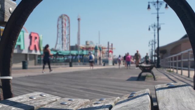 Coney Island beach promenade in Brooklyn, New York, United States. Wooden boardwalk near retro luna park. Amusement park on ocean coast beach. Waterfront summer holiday, people walking on promenade.