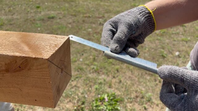 A worker measures a threaded rod with a ruler before inserting it into a wooden beam. DIY construction, and structural assembly projects.