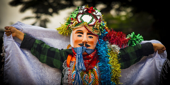 View of a traditional Danzante de los Viejitos dancer wearing an ornate mask with colorful tinsel and a plaid shirt in MICHOACAN, Mexico.