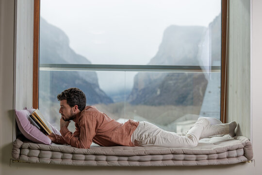 Young man reading a book by a window in a peaceful moment of learning and relaxation