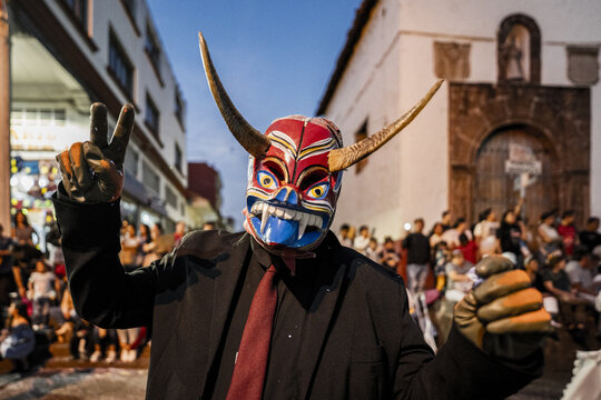 View of a person wearing a traditional Michoacan devil mask with horns and a black suit making a peace sign during a cultural festival in MICHOACAN, Mexico.