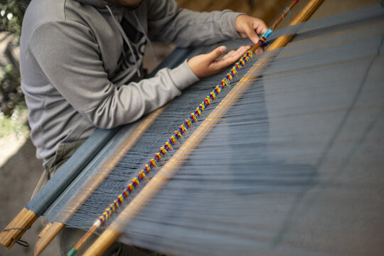 View of a person weaving a traditional Ahuiran reboso on a backstrap loom with intricate blue and colorful threads in Ahuiran, Michoacan, Mexico.