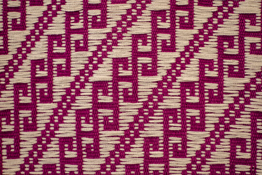 View of the intricate geometric patterns of a traditional Ahuiran reboso textile with magenta and cream threads in Ahuiran, Michoacan, Mexico.