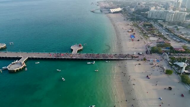 Aerial drone footage captures beautiful turquoise sea beach with pier and white sand on Kish Island under bright daylight showcasing tropical paradise and tourism destination.