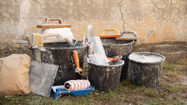 Construction buckets with plaster scraps, trowels, a paint roller, and dry mix outdoors during home renovations and interior finishing work. Cost of home renovations, building materials, and repairs.