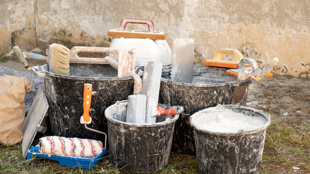 Construction buckets with plaster scraps, trowels, a paint roller, and dry mix outdoors during home renovations and interior finishing work. Cost of home renovations, building materials, and repairs.