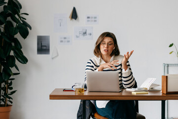The woman speaks in a creative workspace while working on her laptop