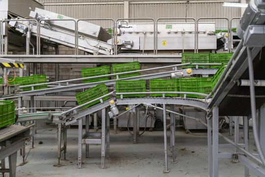 View of an industrial avocado packing house with automated conveyor belts and stacked green plastic crates in Uruapan, Michoacan, Mexico.