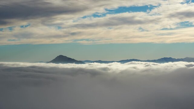 Telephoto Timelapse of Sea of Fog Waving Below Pointy Mountain Peak