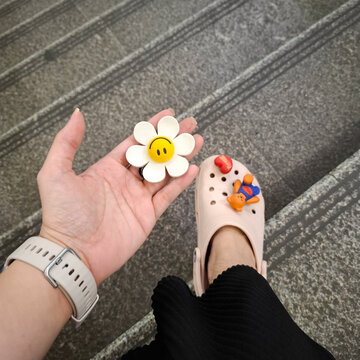 Woman hand holding cute Wiggle Wiggle flower jibbitz accessory wearing Crocs shoes on stairs on August 2, 2026 in Bangkok, Thailand 
