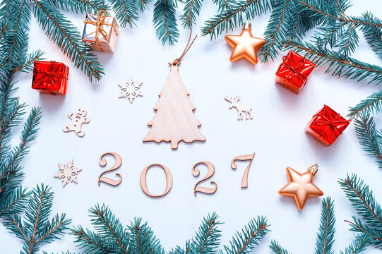 New Year background - 2027 figures, festive Christmas toys, blue fir tree branches on white wooden background. Flat lay, top view
