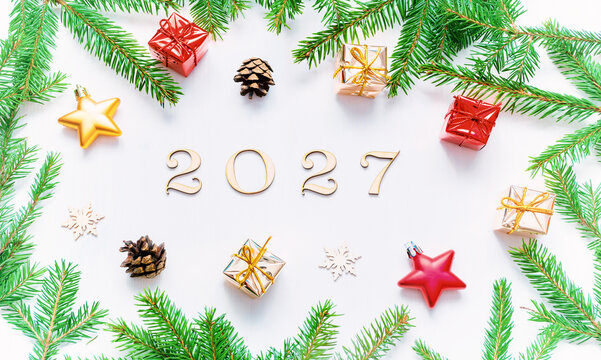 New Year 2027 background - composition with wooden 2027 figures, Christmas toys, green fir branches and fir cones on the white background. Flat lay, top view