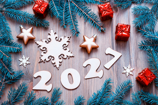 Festive New Year 2027 background - still life made of 2027 figures, Christmas toys, and blue fir tree branches on the rustic wooden background. Flat lay, top view