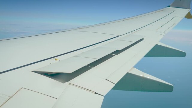 Aircraft wing with raised speed brakes during descent toward landing. Spoilers reducing lift and slowing commercial airplane. Aviation control surfaces above blue sky