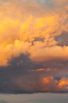 Golden colorful dramatic sunset sky background - picturesque clouds of bright yellow and orange colors lit by evening sunlight, vertical landscape of sky nature