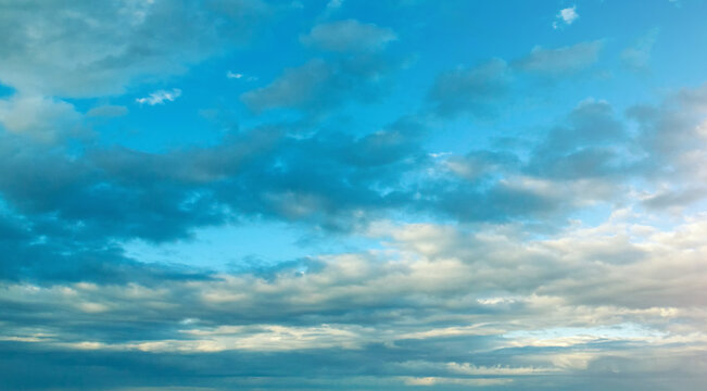 Blue sky panoramic landscape. Fluffy cumulus clouds covering a bright blue sky at sunset time