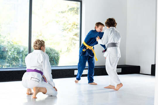 Young judokas practice standing grips while blonde coach watches from mat. Concept of group judo lessons, youth club promotion and peer skill building.