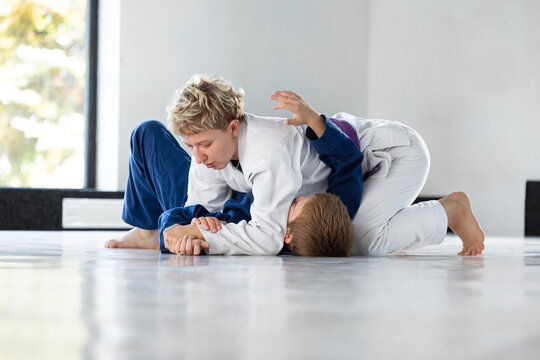 Female judo instructor joins children on mat to demonstrate ground control. Concept of hands-on coaching, beginner grappling classes and instructor education.
